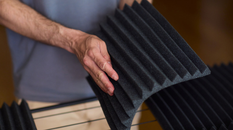 A man holds an acoustic foam panel with other panels laying nearby.