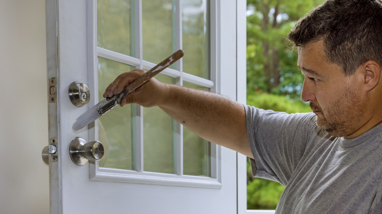A handyman painting the front door of a home.