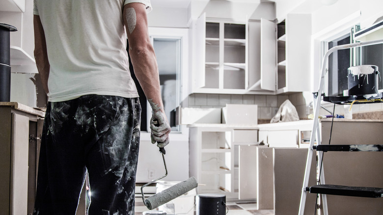 Person holding paint roller facing kitchen cabinets