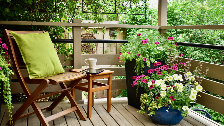 A lovely private garden space on a deck with a wooden chair and small table surrounded by greenery and colorful potted plants