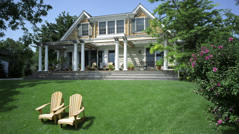 A large house sits on a huge swath of lawn containing two Adirondack chairs.