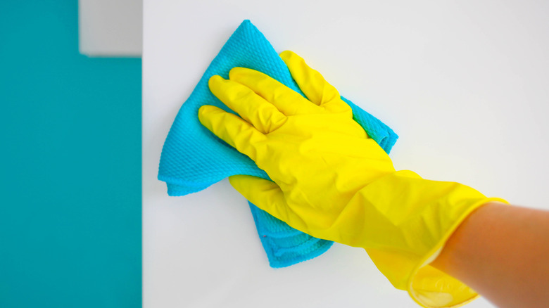 A person wearing a glove cleans a wall with a turquoise rag