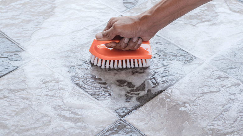 A hand holding a scrub brush, cleaning a tile floor