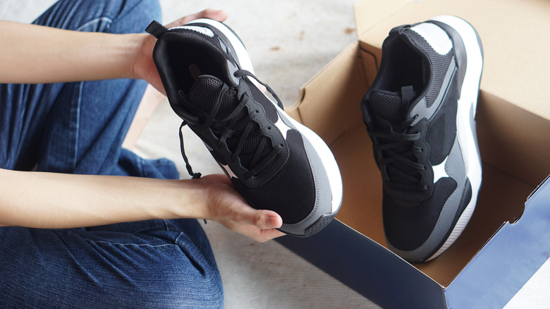 Person holding a new pair of black and white sneakers above the shoebox