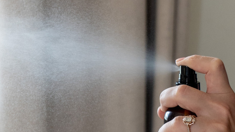 A person sprays curtains with a tea tree oil and water solution.