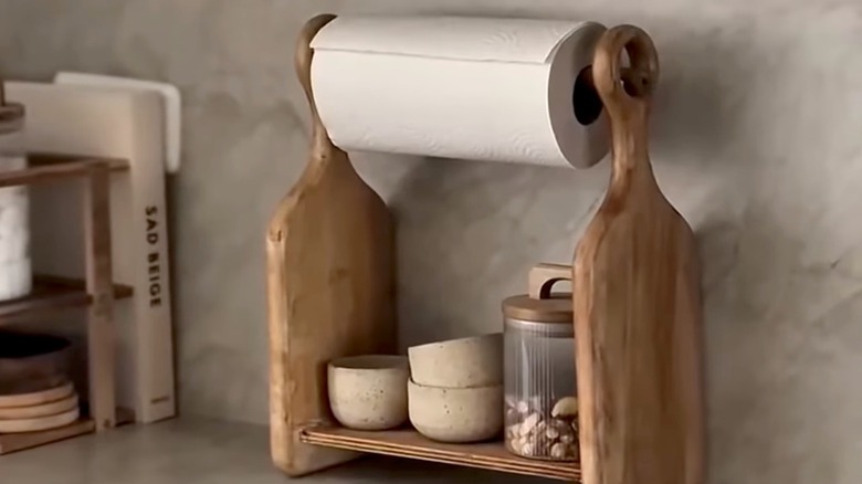 A paper towel dispenser made out of two cutting boards sits on a countertop in a kitchen.