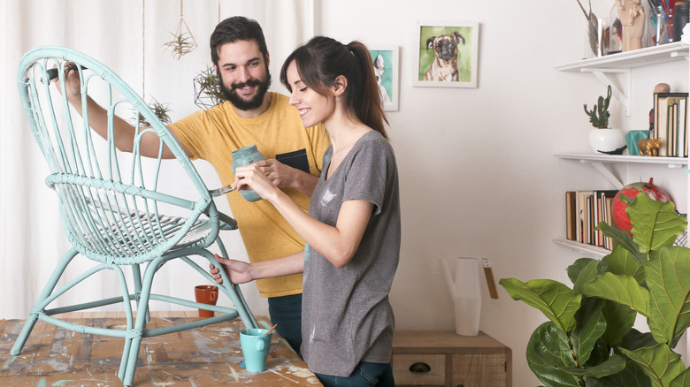 Man and woman painting a wicker chair