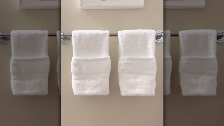 Two neatly folded white hand towels hang on a rack in a bathroom.