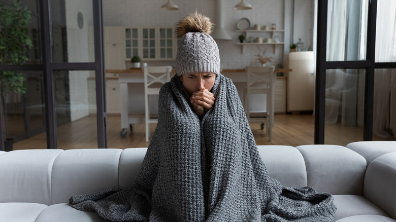 A woman sitting in a chilly house covered in a blanket