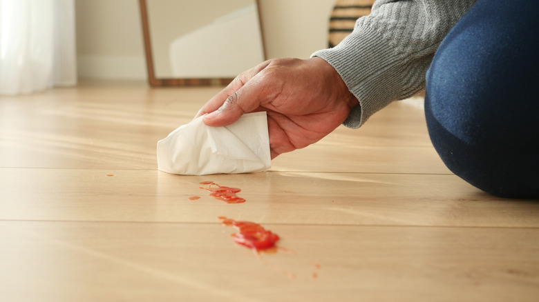 A man's hand trying to wipe ketchup from hardwood floors