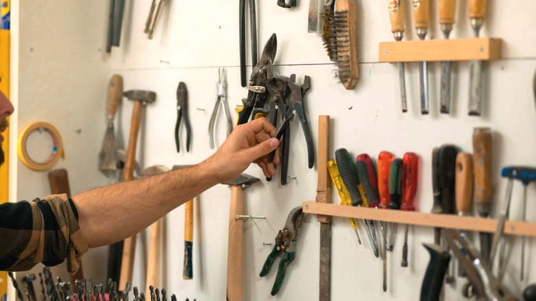 A person reaching for equipment on a workshop wall of hand tools