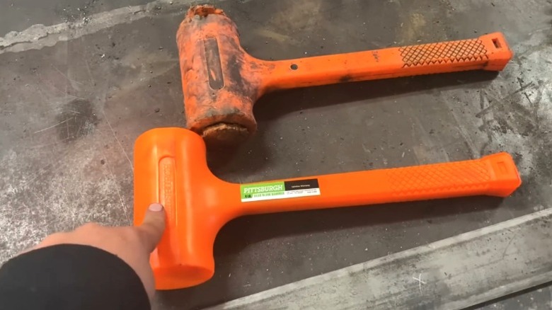 Person pointing at new Pittsburgh dead blow hammer next to worn hammer on metal surface