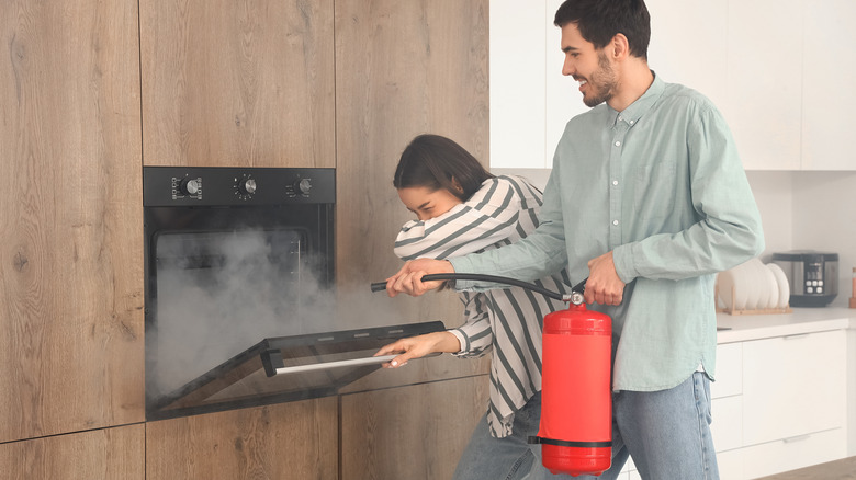 young couple extinguishing oven fire with extinguisher
