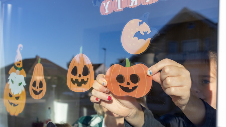 Person decorating for Halloween with pumpkin stickers on a window