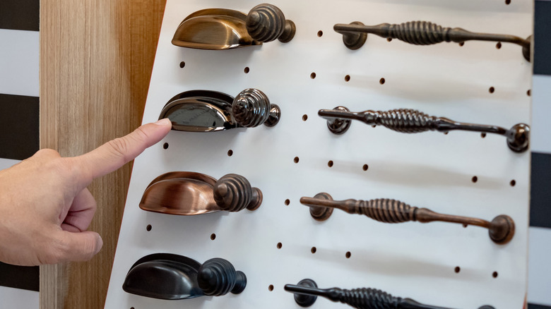 A hand pointing at bronze cabinet pulls.