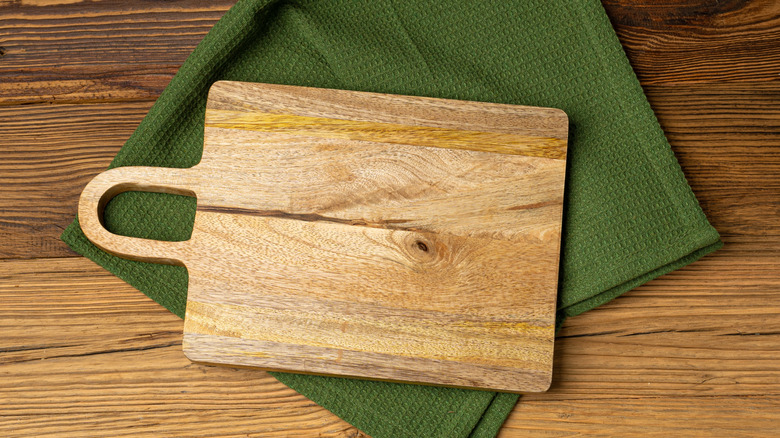 A wooden cutting board lying on a green cloth on a rustic shelf