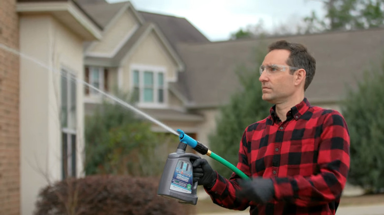 Man holding sprayer uses hose to spray Wet and Forget