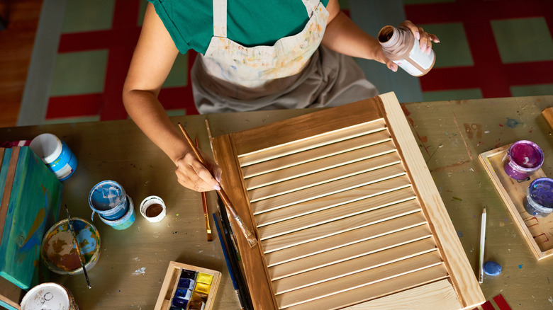 Woman painting plain wood shutter brown.