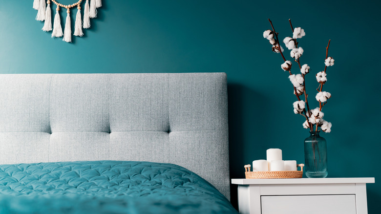 Bedroom with teal walls and bedding with light-colored headboard