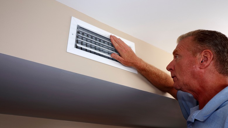 man checks heat at vent