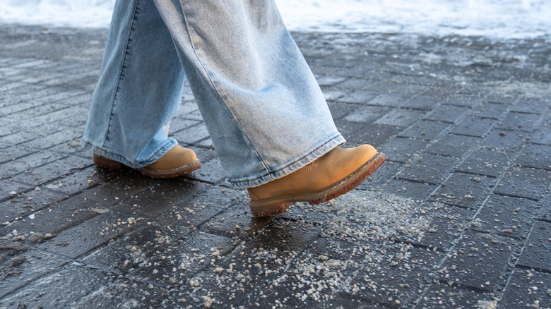 A person wearing jeans and boots walking through de-icing salt on a brick sidewalk