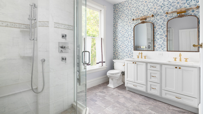 Bathroom with tile wall and floor, white cabinets, and blue and white wallpaper