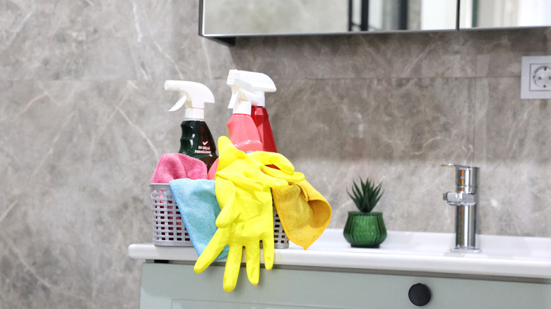 Marble bathroom with a basket of cleaning supplies and yellow gloves on the countertop