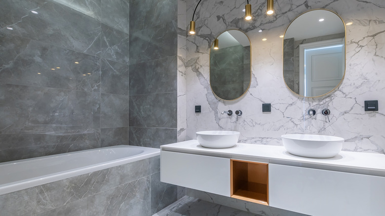 Bathroom with gray and white marble, white sinks, and oval mirrors