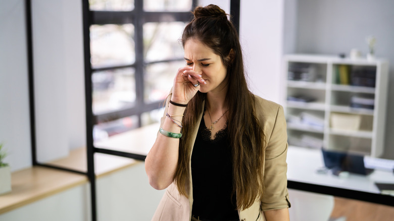 Woman holding her nose as she walks into the room, smelling a bad odor.