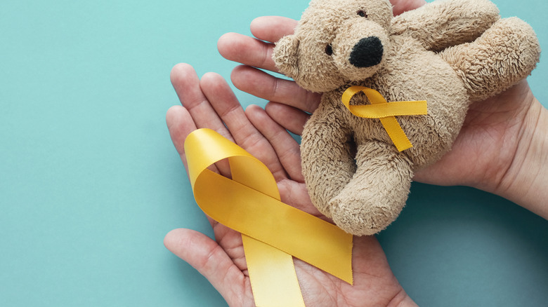 Person holding gold ribbon and teddy bear for childhood cancer awareness