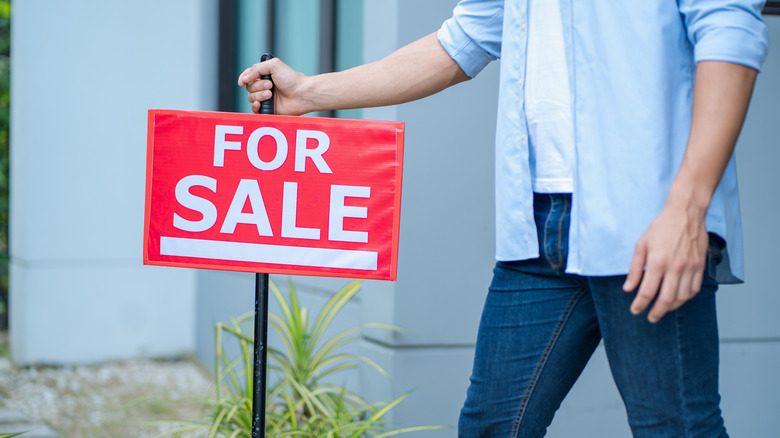 A man posting a for sale sign in a yard.