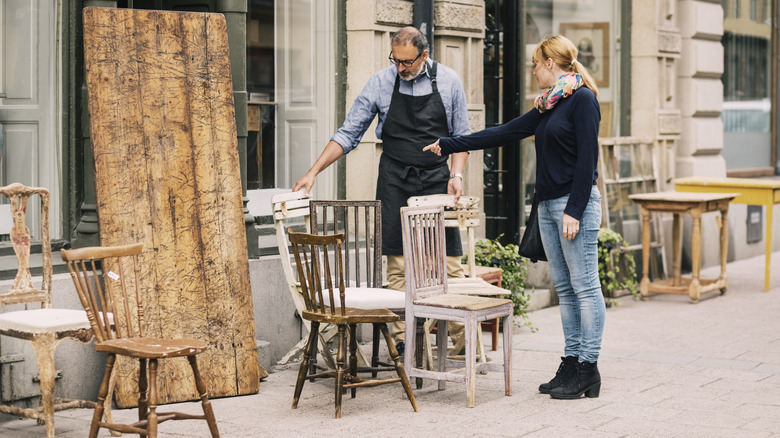A shopper and an employee looking at old chairs for sale outdoors