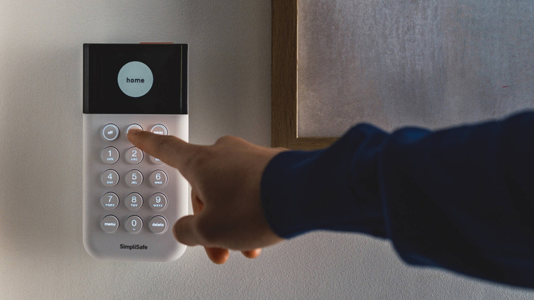 Hand reaching out to push a button on a SimpliSafe base unit