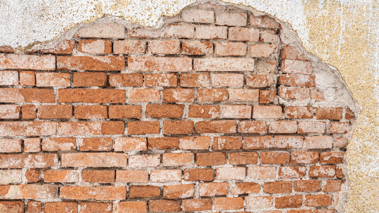 Old brick wall behind crumbling stucco veneer