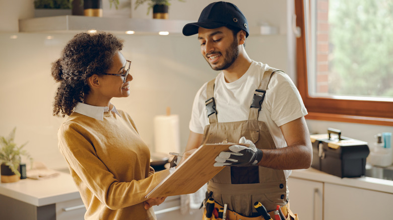 Woman signing contract with repairman in home kitchen