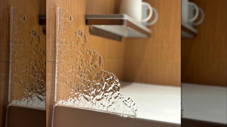 Corner-shaped clear decorative splash guard beside a sink.