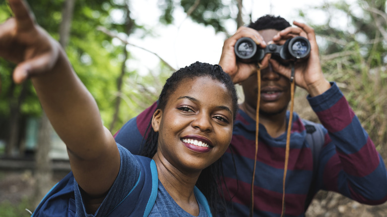 A man with binoculars and woman pointing while bird watching