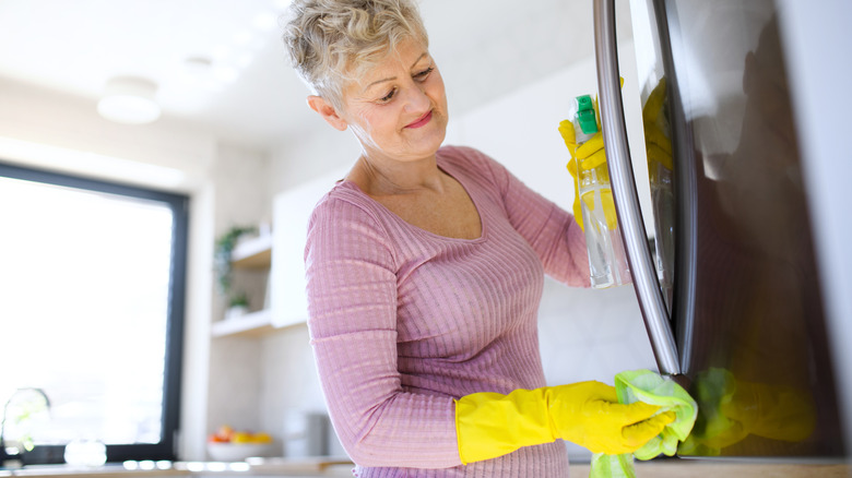 A mature person wipes down a stainless steel refrigerator