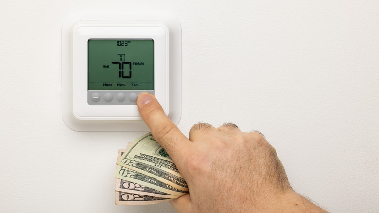 Someone holding cash while adjusting their thermostat.