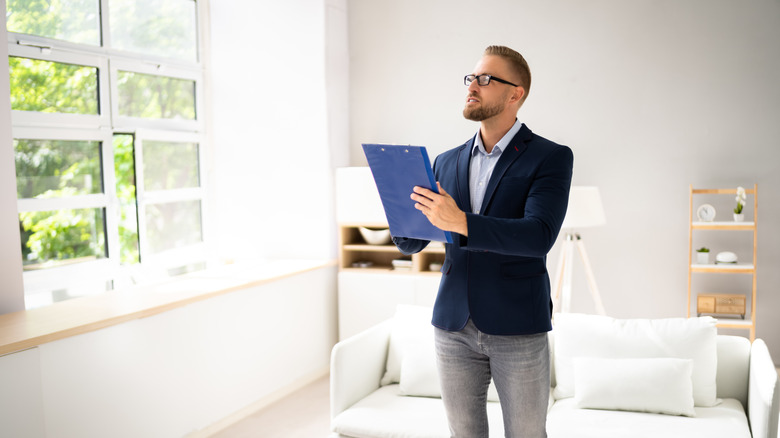 A man holds a clipboard while appraising a house
