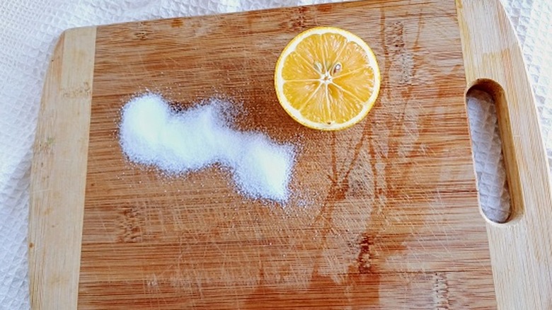 A close-up image of salt and half a lemon on a wooden cutting board