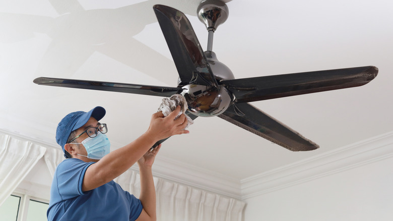 man cleaning a ceiling fan wearing a mask