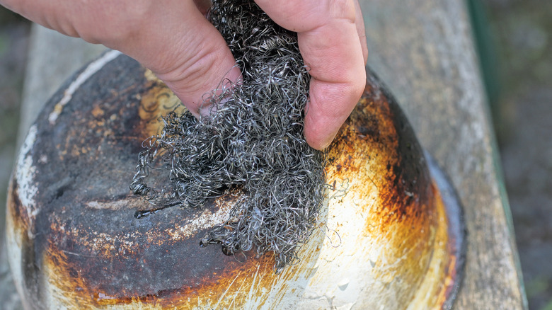 A hand scrubbing a pot with steel wool