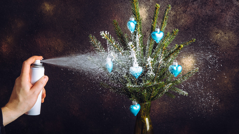 Hand spraying fake snow on greenery