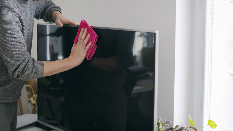 Close-up of person cleaning a TV screen with a pink cloth.