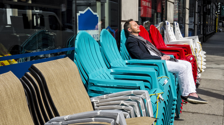 A man sitting on a stack of plastic outdoor chairs for sale