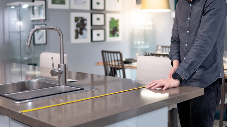 A person measures their island countertop and overhang.