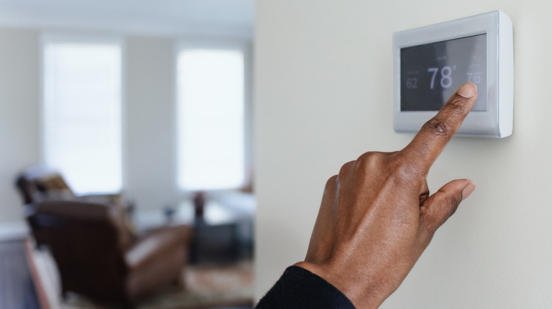 A person's hand setting a smart thermostat, which is located on a wall and unobstructed.