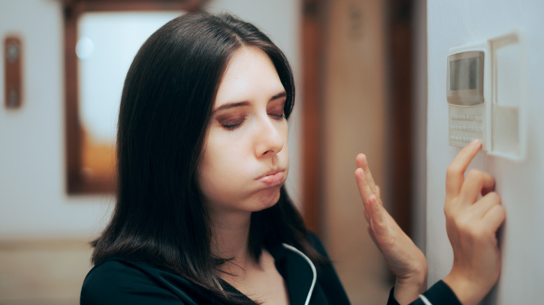 Woman adjusting her thermostat during summer while expressing that she's hot by blowing air from her mouth.