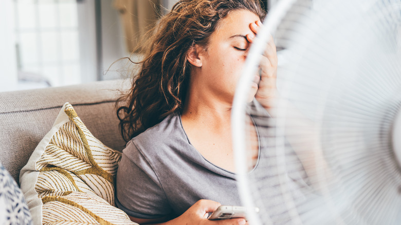 A woman sits in front of a fan and cools herself